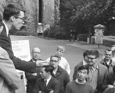 A photo of a crowd of men gathered on University of Pennsylvania's campus outside on Locust Walk. Young Kiyoshi is in the crowd looking up at a speaker.
