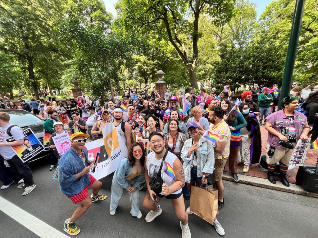A photo of a large crowd of people standing on a city street and wearing rainbow pride outfits and accessories