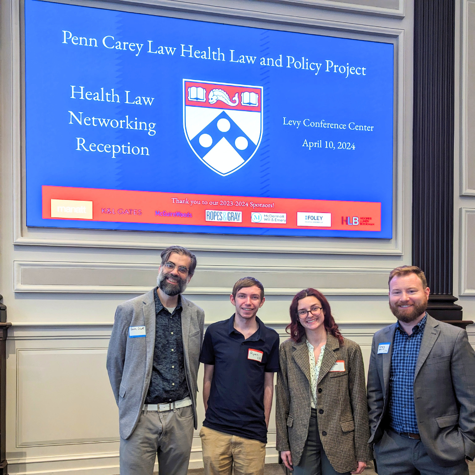 Photo of Kevin Schott standing beside three Penn Carey Law students in front of a large screen reading "Penn Carey Law Health Law and Policy Project: Health Law Networking Reception."