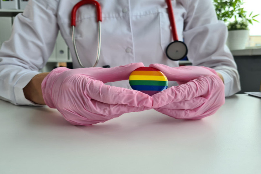Photo of a physician in a lab coat holding a rainbow pride pin with gloved hands